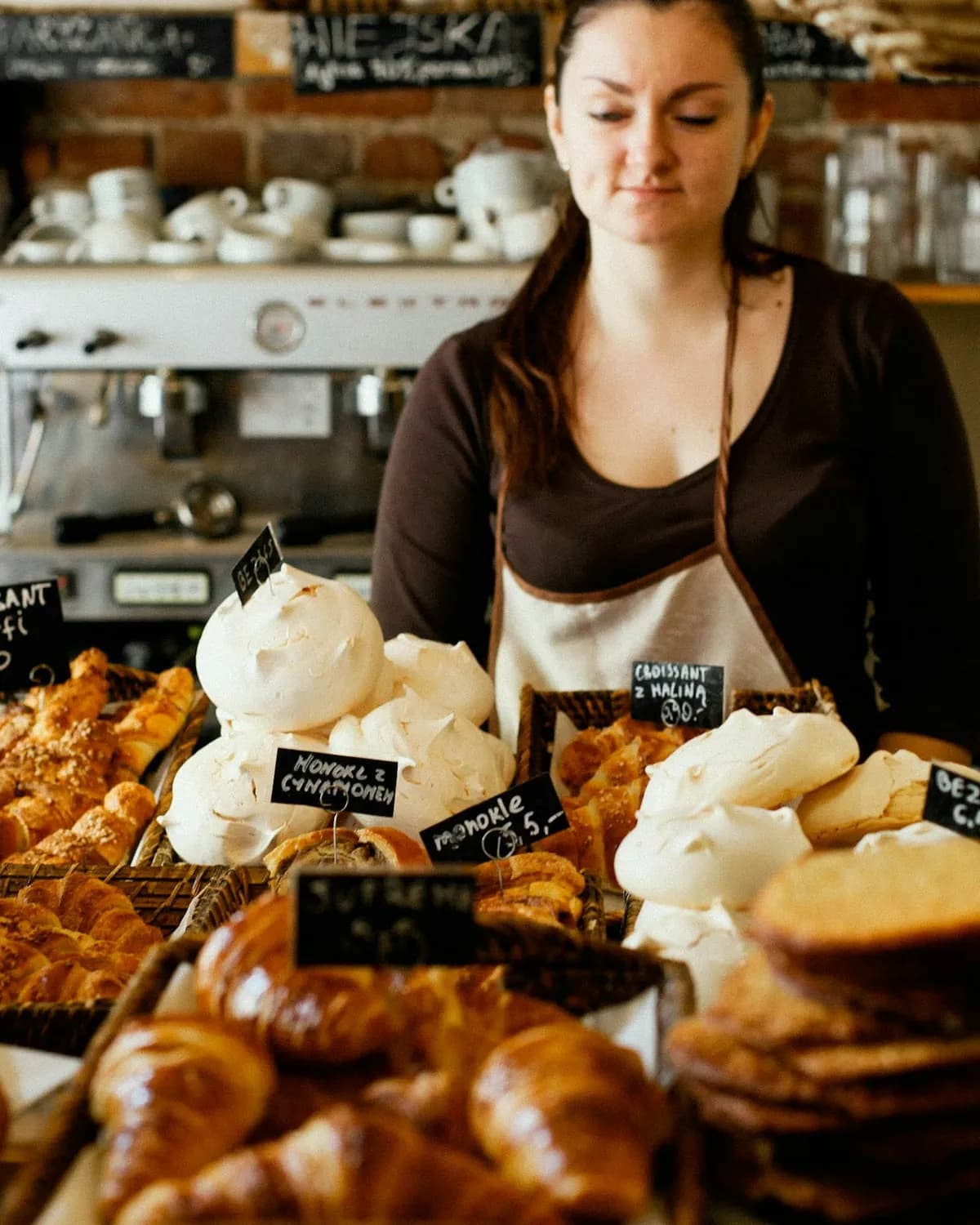 A baker arranging croissants and meringues behind a café counter