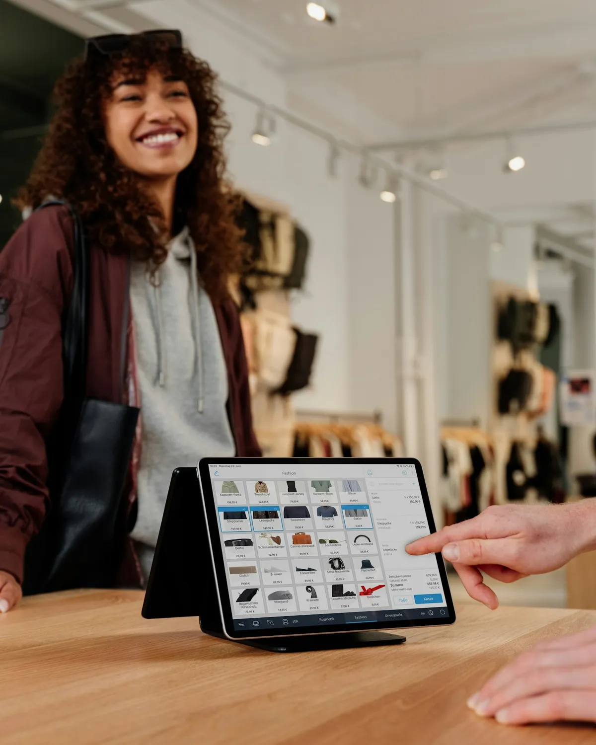 A smiling customer at a clothing store counter as the assistant rings up her order on a tablet