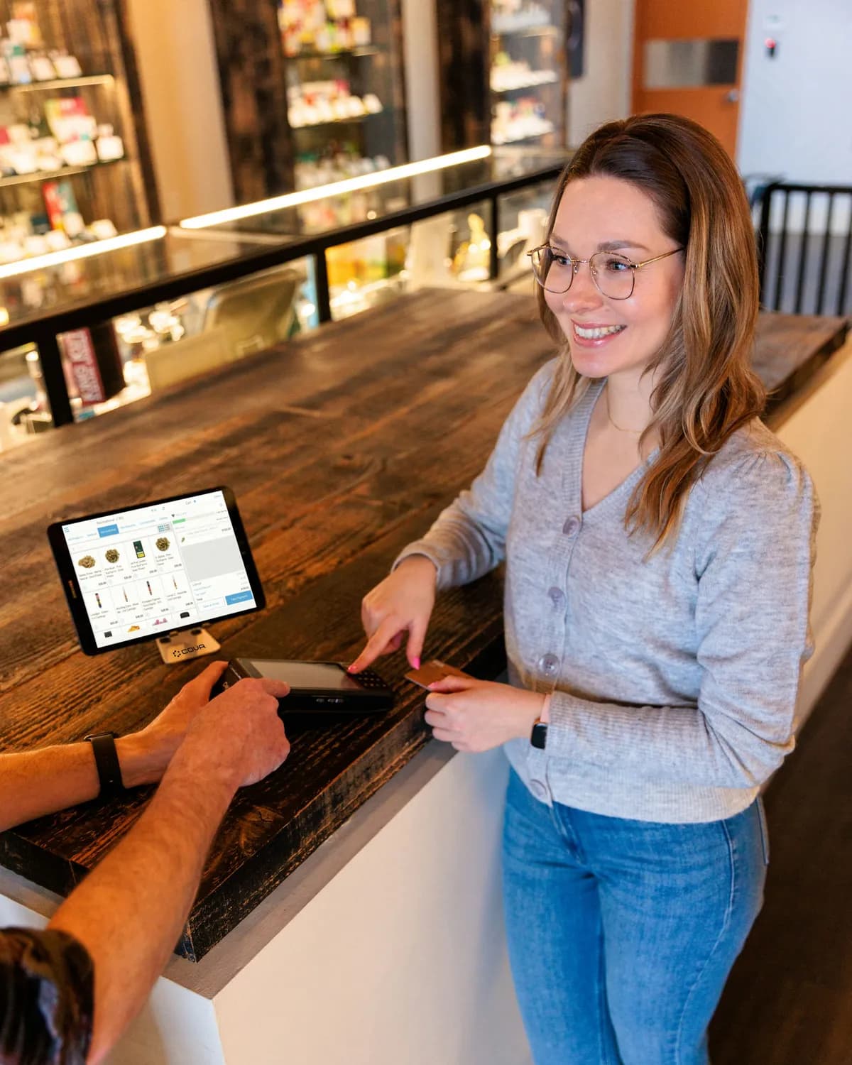 A smiling server at a café counter as a customer pays beside a tablet point-of-sale