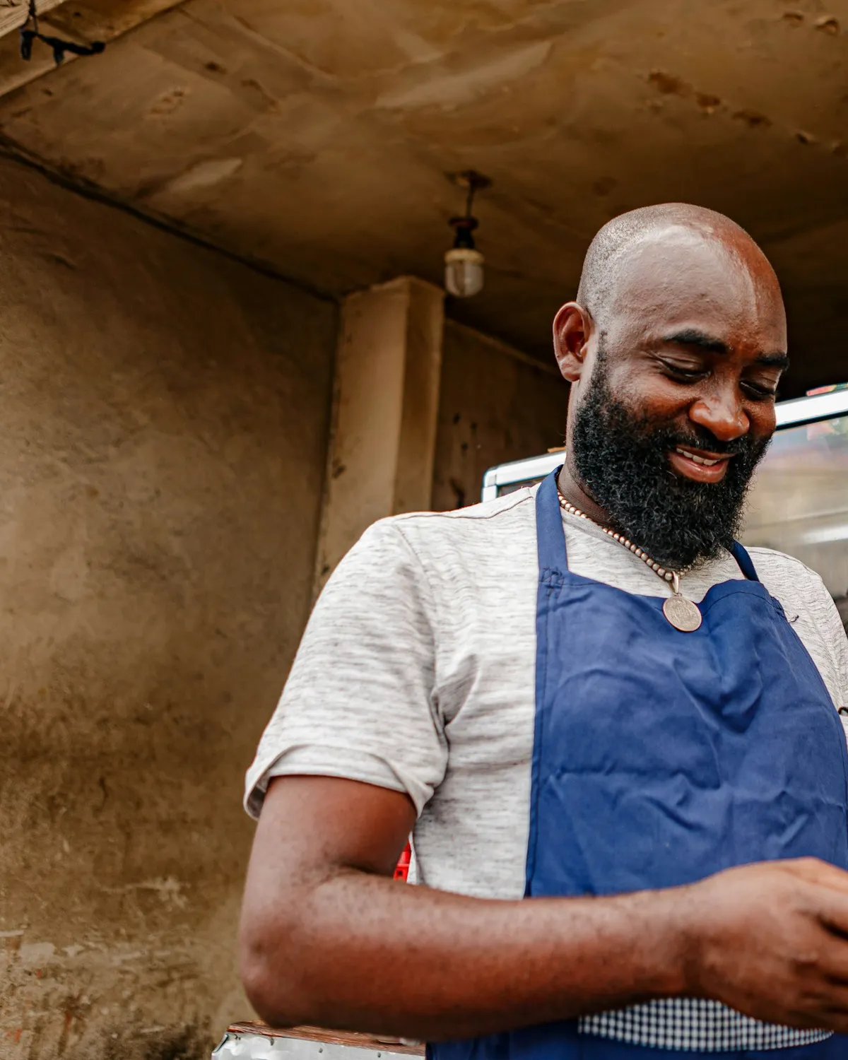 A smiling deli owner in a blue apron checking his phone behind the counter