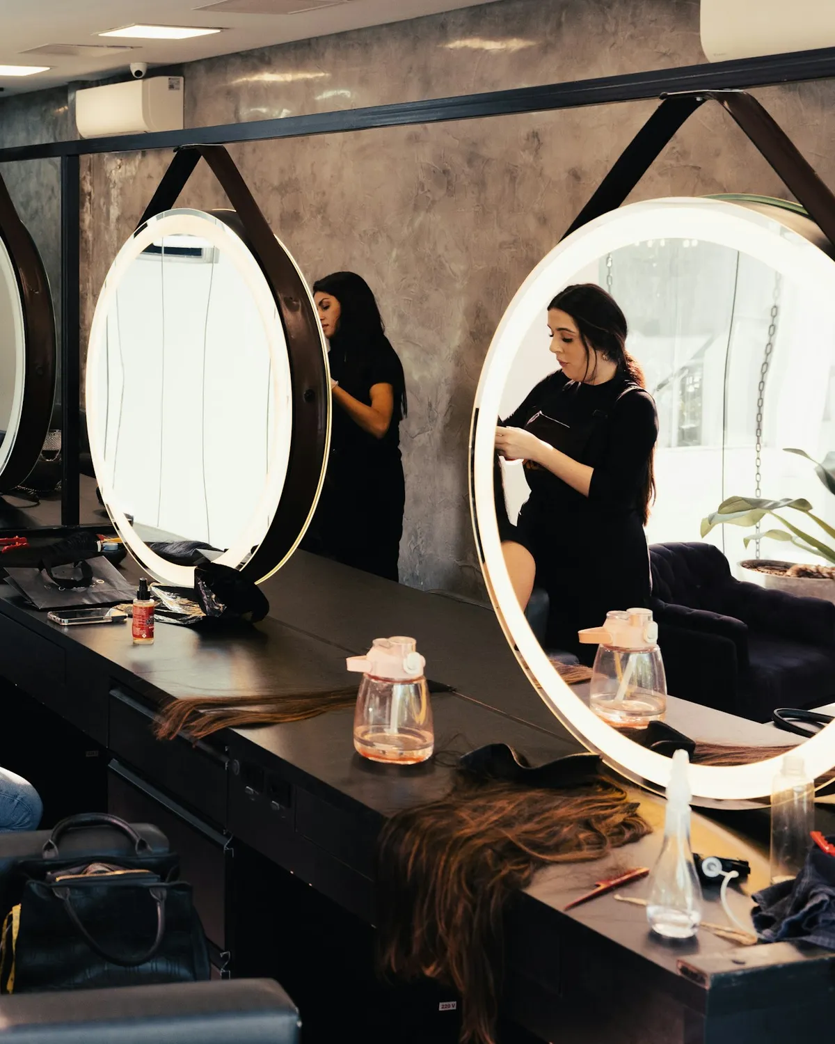 Stylists at work in front of round lit mirrors in a hair salon