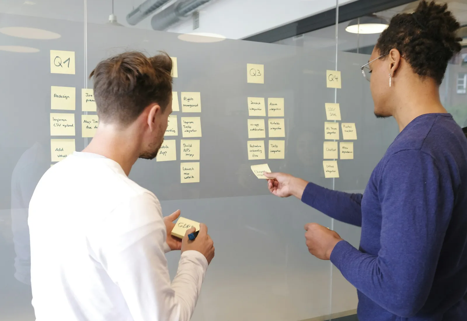 Two people mapping a process on a glass wall covered in sticky notes