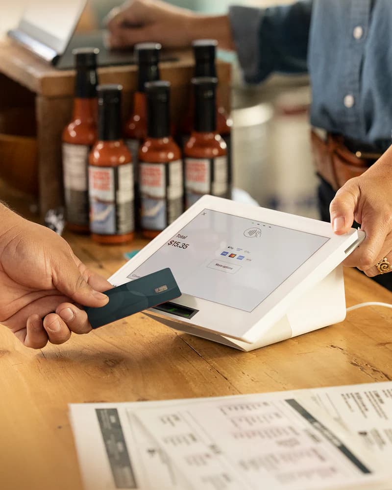 A customer inserting a card into a Clover Mini on a counter stand at a hot sauce stall
