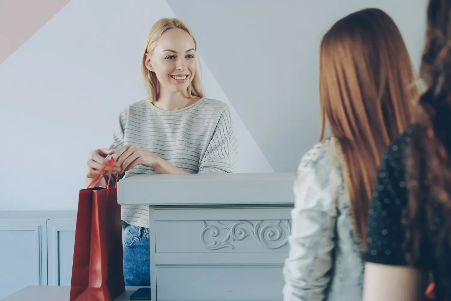 A shop assistant smiling as she hands a shopping bag across the counter to a customer