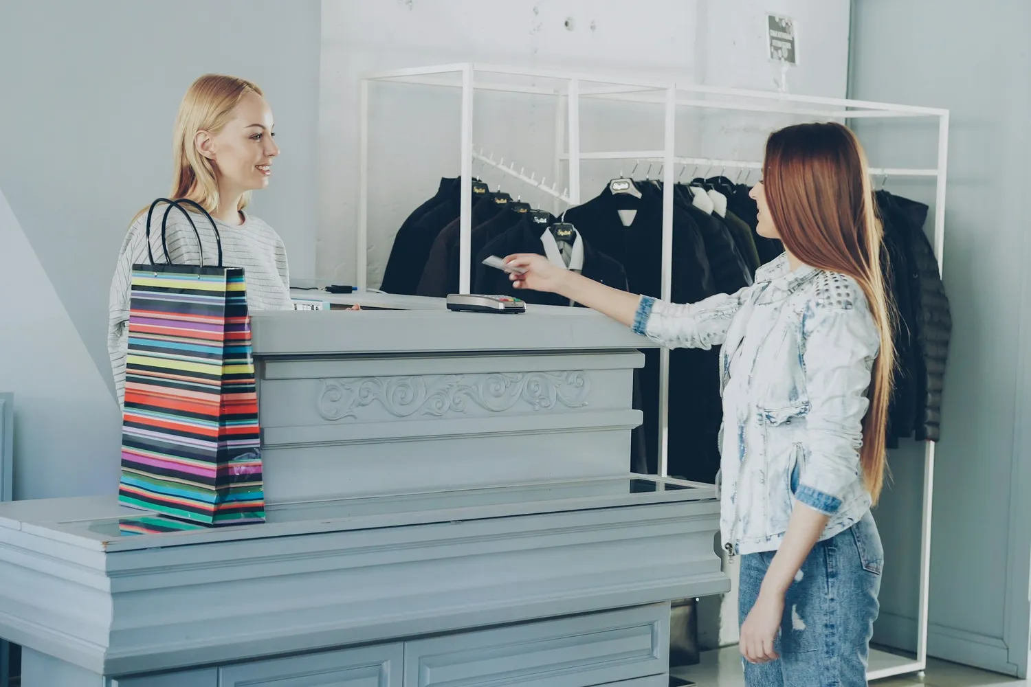 A customer paying at a boutique checkout counter beside a striped shopping bag