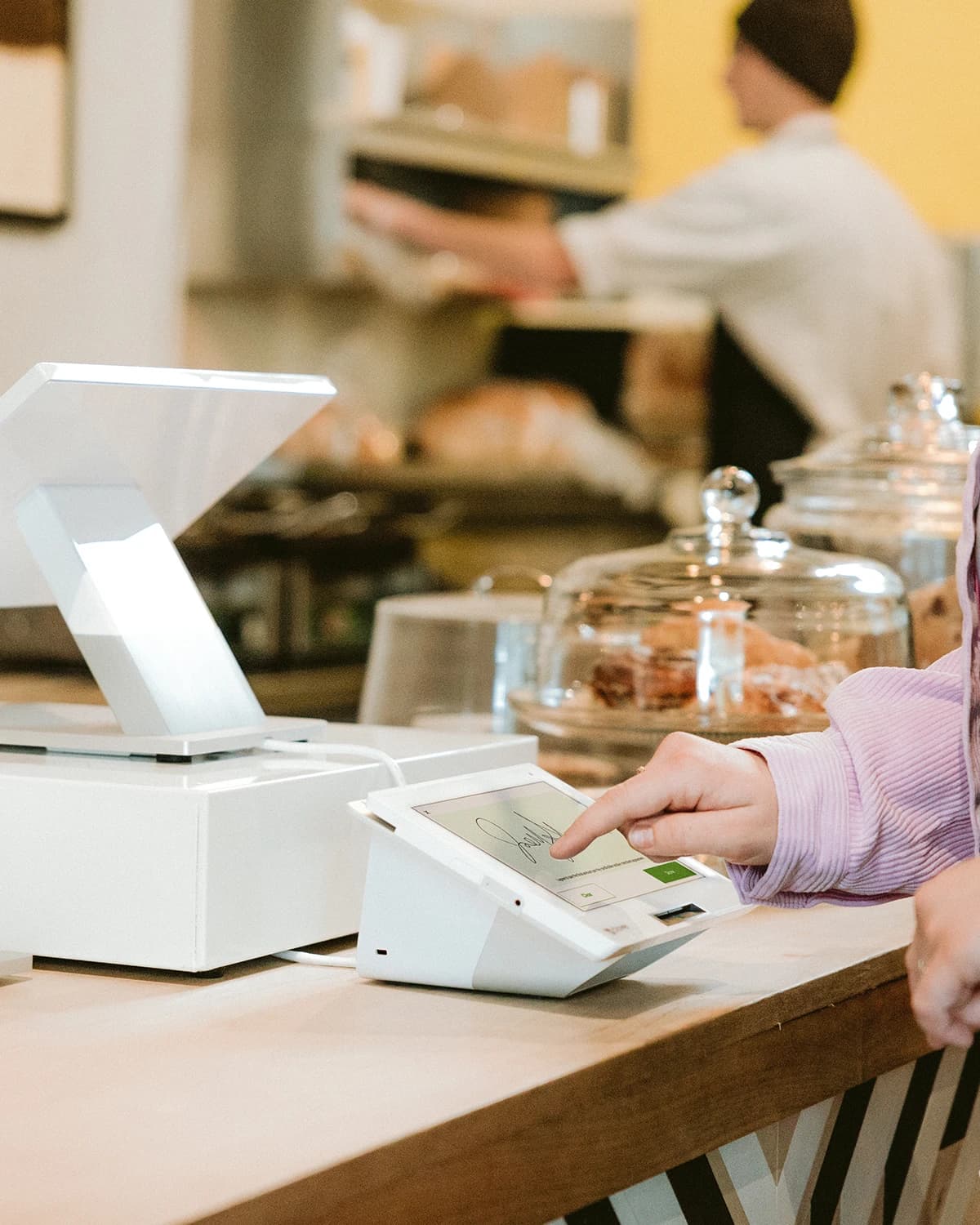 A customer paying at a bakery counter beside glass jars of pastries