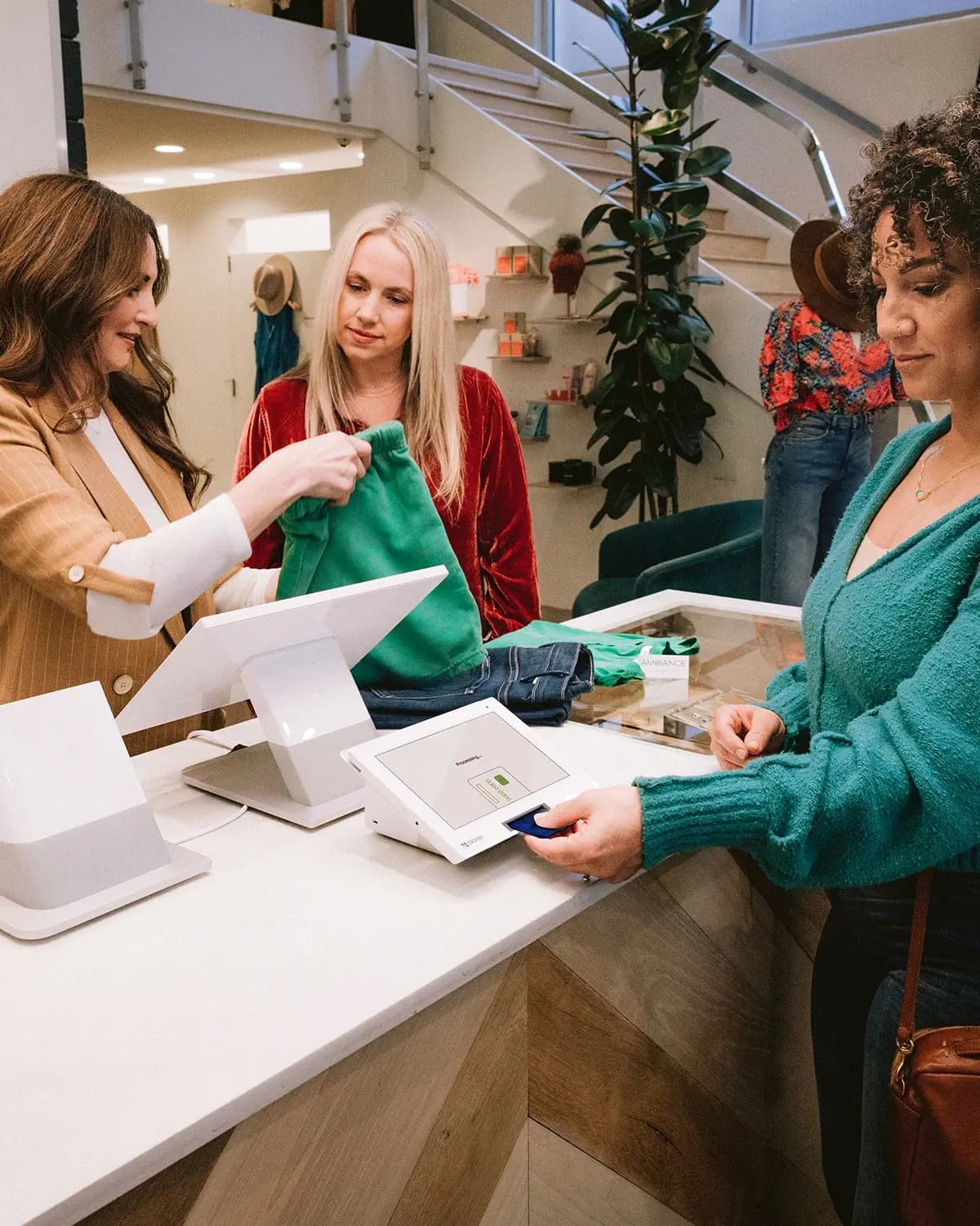 A shop assistant handing a bag to a customer paying by card in a boutique